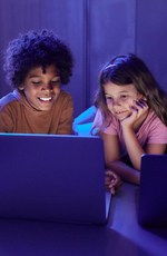 Two elementary school children look at laptops during class